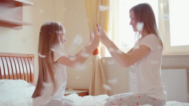 Cute daughter and mother sitting on the bed and playing Okay play. Among the fluff and feathers. Slowmotion — Αρχείο Βίντεο