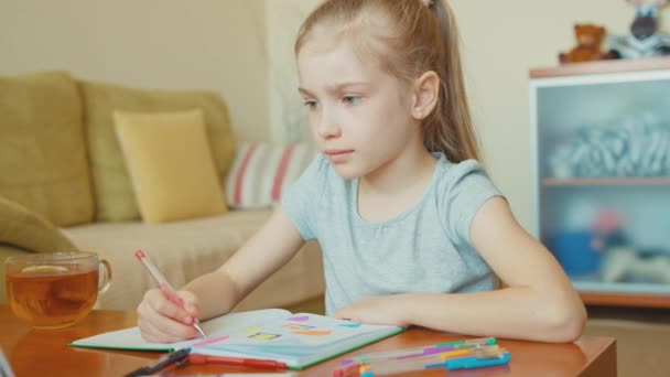 Meisje 7 jaar oude tekening in een notitieblok en lachend op camera — Stockvideo