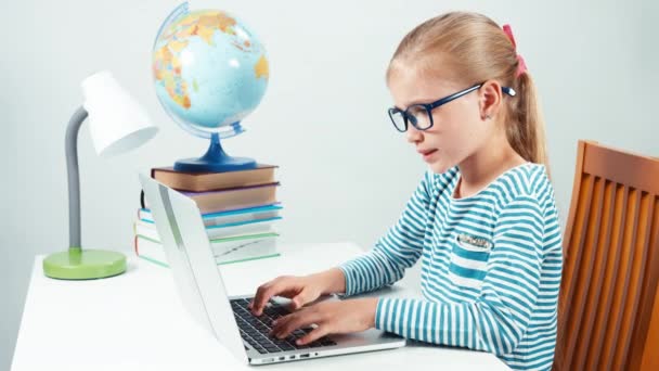 Portret 7-8 jaar schoolmeisje in glazen met behulp van laptop en glimlachend in de camera. Meisje geïsoleerd op wit — Stockvideo