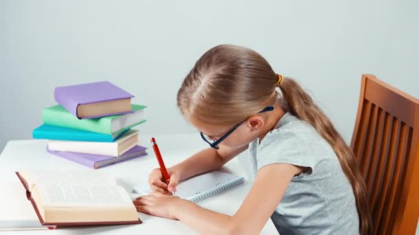 Porträt Studentin Mädchen 7-8 Jahre alt mit Brille etwas schreibend in ihr Notizbuch und Blick in die Kamera. Ansicht von oben — Stockvideo