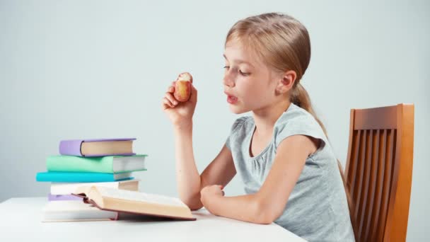 Portrait student girl child 7-8 years reading textbook and eating fruit. Isolated — Stockvideo