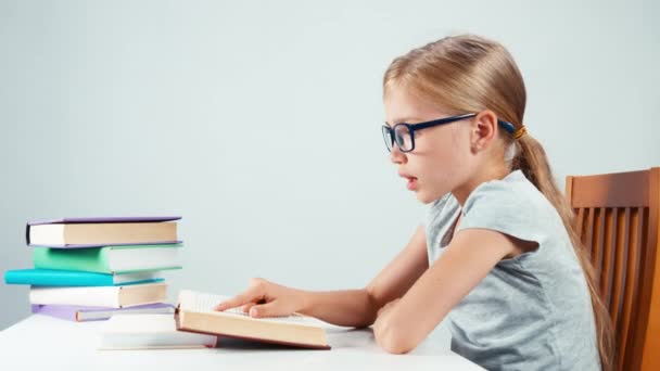 Primer plano retrato estudiante niña 7-8 años leyendo libro y sonriendo a la cámara con los dientes. Aislado sobre blanco — Vídeo de stock