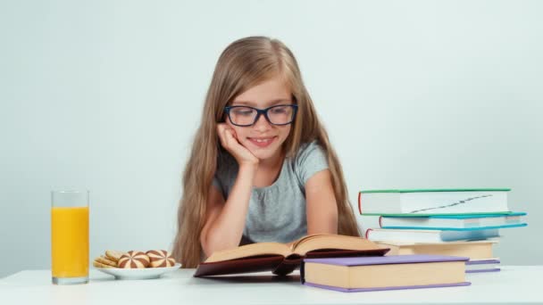 Porträt glückliches Schulmädchen mit Brille, das Lehrbuch auf dem Tisch liest und mit Zähnen in die Kamera lächelt — Stockvideo