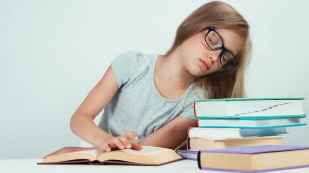 Schoolgirl lying on the stack of books wakes up and saddly reading textbook — Stock video