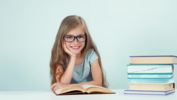 Nahaufnahme Porträt Schulmädchen streckt sich vor der Kamera und liest Buch am Tisch isoliert auf weiß — Stockvideo