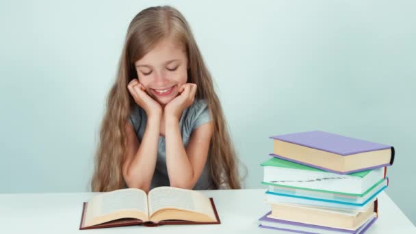 Happy schoolgirl 7-8 years old reading book on the table and looking at camera on white background — Αρχείο Βίντεο