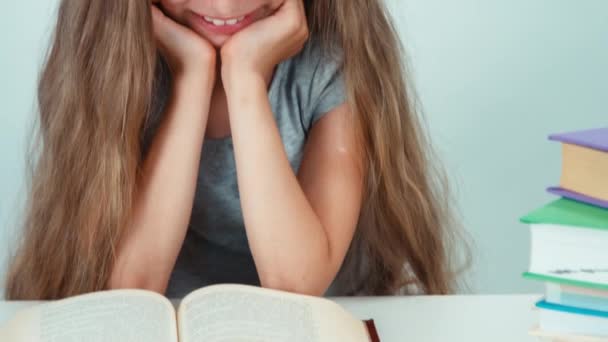 Primer plano retrato colegiala lectura libro en la mesa. Sobre fondo blanco. Niño sonriendo a la cámara — Vídeos de Stock