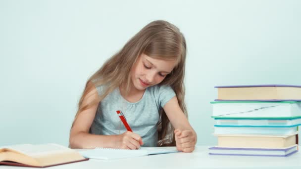 Close up portrait schoolgirl something writing in her school notebook on white background. Child girl sitting at the desk and smiling at camera — Stockvideo