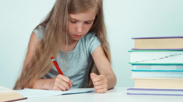 Крупним планом портрет школярки вивчає уроки на білому тлі. Дитяча дівчина сидить за столом — стокове відео