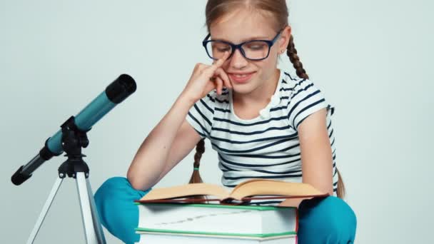 Close up portrait girl 7-8 years old reading book near telescope. Panning — Αρχείο Βίντεο