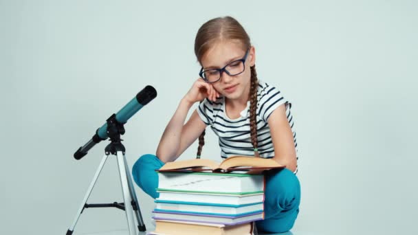 Retrato niña 7-8 años de edad libro de lectura cerca del telescopio y sentado cerca de él y sonriendo con los dientes en la cámara aislada en blanco — Vídeos de Stock