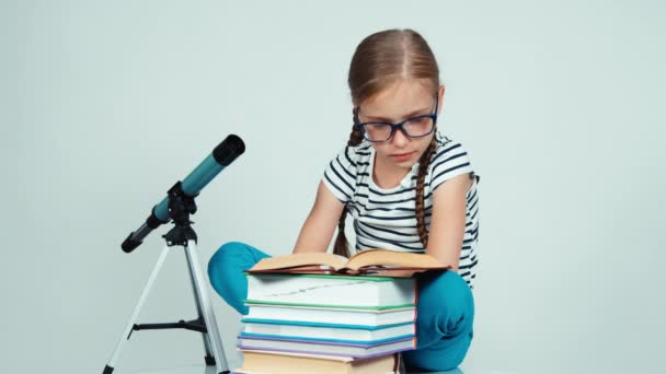 Portrait girl 7-8 years old reading book near telescope and sitting near it and smiling with teeth at camera — Stock Video