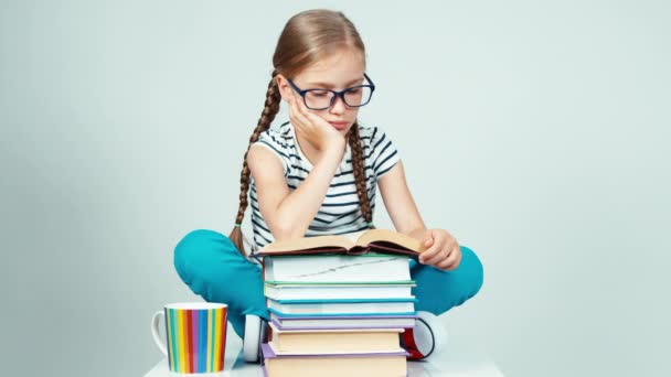 Девочка 7-8 лет в очках читает книгу и улыбается в камеру с зубами на белом фоне — стоковое видео