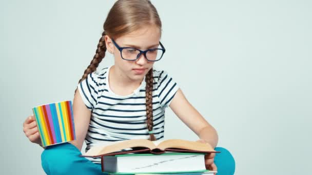 Bliska portret Ładna dziewczyna 7-8 lat, które czytanie książki i gospodarstwa filiżankę herbaty. Dziecko uśmiecha się do kamery z zębami na białym tle — Wideo stockowe