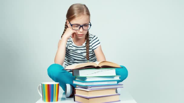 Portret meisje 7-8 jaar oud in glazen lezen boek en glimlachend in de camera. Kind zittend op de vloer geïsoleerd op wit — Stockvideo
