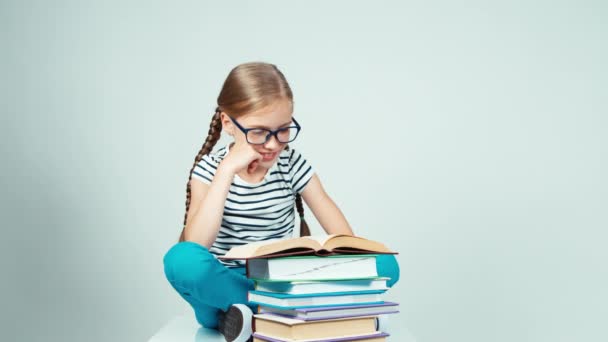 Écolière étirant et lisant un livre et souriant à la caméra assise sur le sol — Video