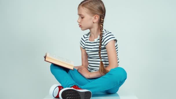 Portrait girl reading a book sitting on the floor and looking at camera — Stock video