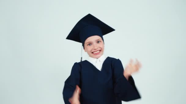 Portrait heureuse étudiante diplômée fille 7-8 ans en manteau se réjouit et souriant avec des dents sur fond blanc — Video