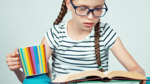 Nahaufnahme Porträt Mädchen 7-8 Jahre alt Buch lesen und halten Tasse Tee isoliert auf weiß — Stockvideo