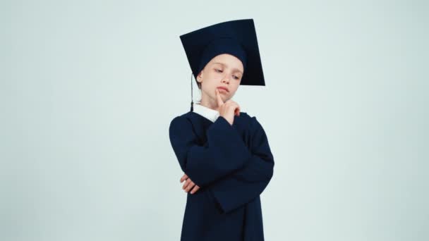 Gros plan portrait diplômée fille 7-8 ans dans le manteau et chapeau penser à quelque chose — Video