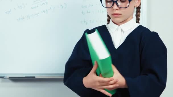 Little student opening book. Close up portrait smiling graduate in the mantle standing near whiteboard in the classroom and looking at camera — ストック動画