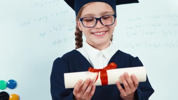 Крупним планом портрет маленької студентки випускник мантії, що показує диплом на камеру і посміхається зубами — стокове відео
