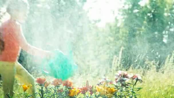 Girl child 7-8 years old holding watering can for flowers running around flowers — Αρχείο Βίντεο