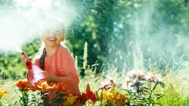 Girl playing with sprinkler near flowers in the garden and smiling — Stockvideo