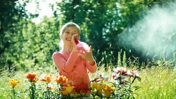 Ritratto ragazza spruzzatore suoi fiori in giardino e sorridente alla macchina fotografica — Video Stock