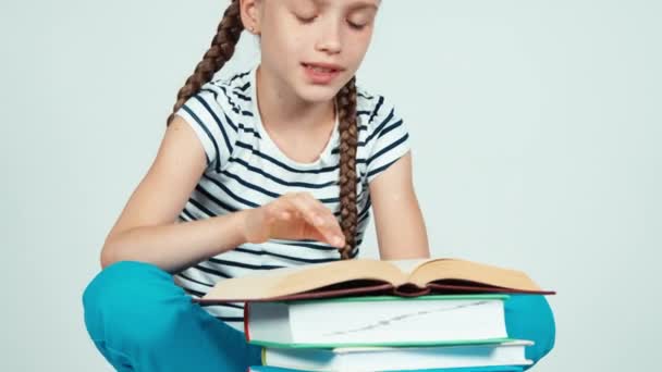 Primer plano retrato riéndose niña leyendo libro y sonriendo a la cámara con los dientes sobre fondo blanco — Vídeo de stock