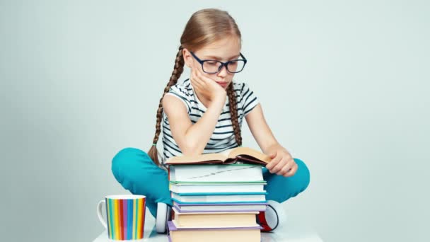 Chica 7-8 años en gafas de lectura libro y sonriendo a la cámara con los dientes aislados en blanco — Vídeos de Stock