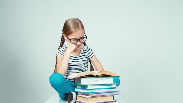 Primer plano retrato 7-8 años niña leyendo libro y sonriendo a la cámara con los dientes sobre fondo blanco. Estiramiento del niño — Vídeos de Stock