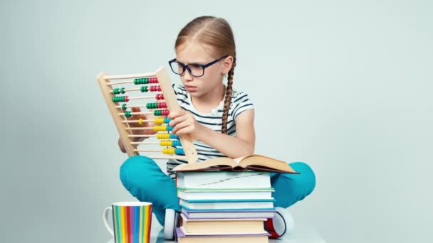 Portrait girl 7-8 years old using abacus and sitting near stack of books and smiling — Stock Video