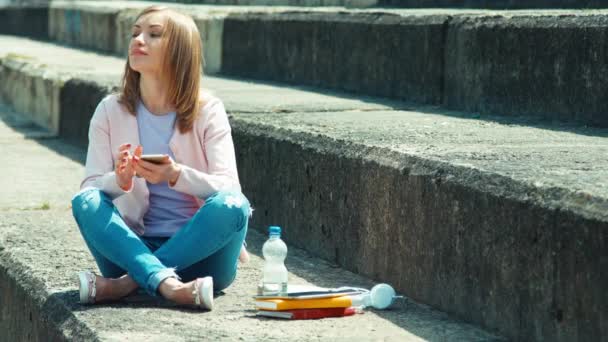 Hermosa estudiante usando su teléfono celular y sonriendo a la cámara — Vídeos de Stock