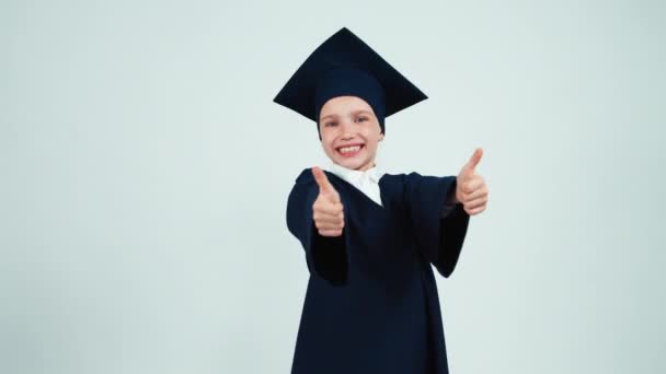 Gros plan portrait jeune fille diplômée mignonne 7-8 ans dans le manteau et le chapeau. Levez le pouce. D'accord. — Video