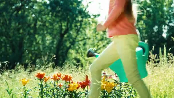 Flickor 7-8 år gammal håller vattenkanna för blommor springer runt blommor och ler mot kameran — Stockvideo