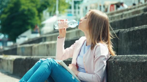 Young woman reading your book and sitting on city quay and drinking water — Stock Video