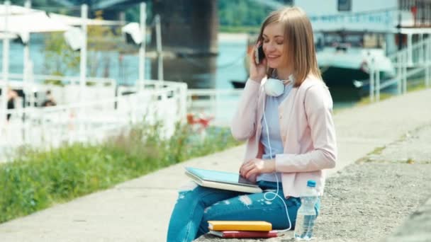 Junge erwachsene Frau, die im Freien mit dem Handy und Tablet-PC spricht und in die Kamera lächelt — Stockvideo