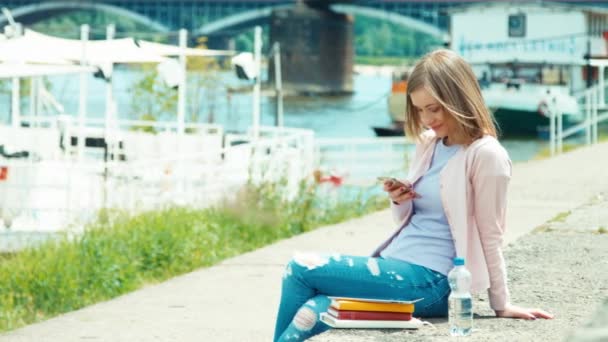 Adulto joven usando teléfono móvil al aire libre cerca del río. Sonriendo a la cámara — Vídeos de Stock