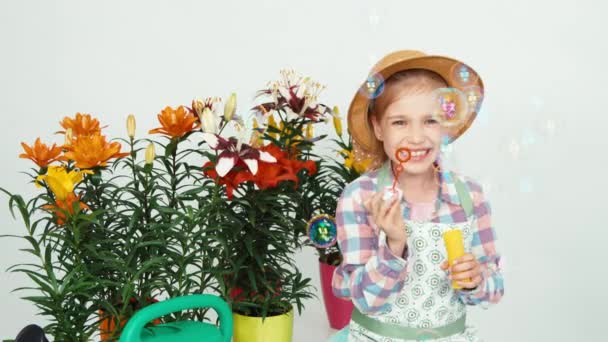 Flor menina criança em chapéu soprando bolhas de sabão na câmera e sorrindo com dentes no fundo branco — Vídeo de Stock