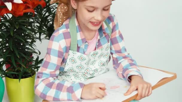 Detailní portrét dítě dívka sedící poblíž květiny a kreslení motýl — Stock video