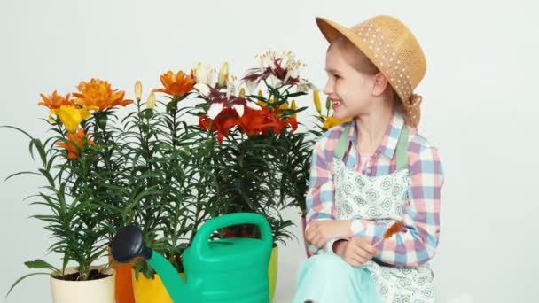 Närbild porträtt blomma-flicka sitter nära blommor och vattenkanna, hålla lollipop och viftande hand på kameran — Stockvideo