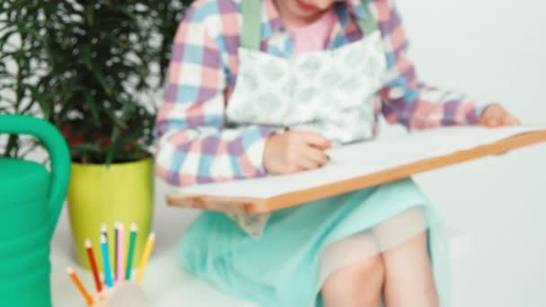 Primer plano retrato niña sentado cerca de flores y dibujo en el tablero de dibujo — Vídeos de Stock