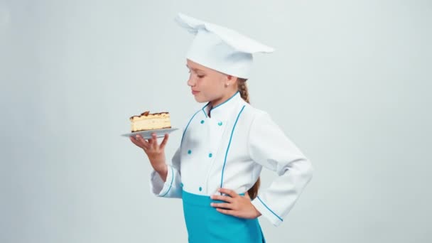 Baker holds chocolate biscuit and examining it. Chef 7-8 years sniffing cake and smiling at camera. Isolated on white background. Thumb up. Ok — Stock Video