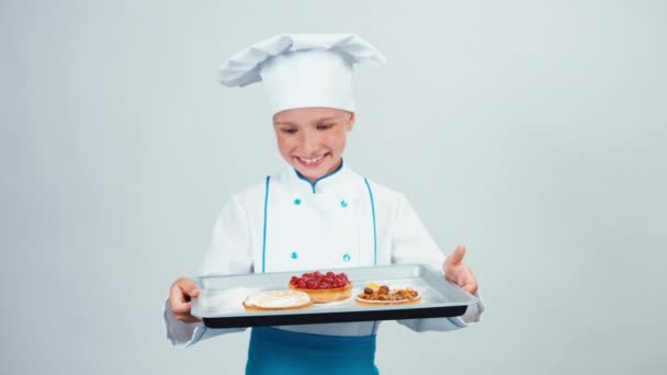 Baker tient le four-plateau avec trois petits gâteaux et souriant à la caméra isolée sur fond blanc — Video