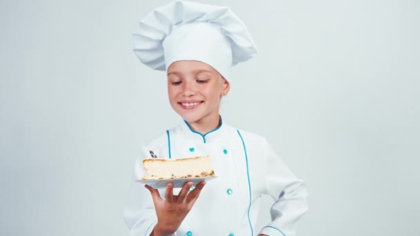 Baker segura um pedaço de cheesecake e dá-lhe. Chef 7-8 anos sorrindo para a câmera. Isolado sobre fundo branco — Vídeo de Stock