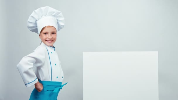 Kuchař kuchař dítě 7-8 let, ukazující na tabuli a usmívá se na fotoaparát s zuby. Izolované na bílém — Stock video
