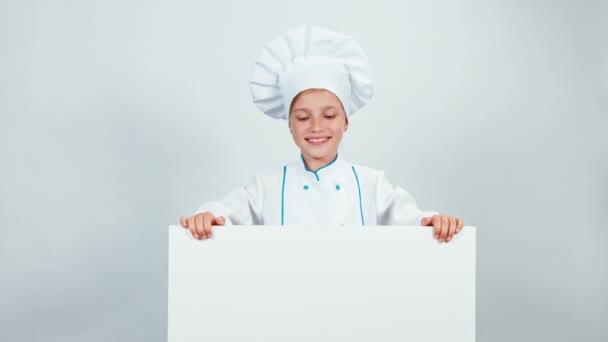 Chef cuisinier enfant 7-8 ans debout derrière le tableau blanc et souriant à la caméra avec des dents. Isolé sur fond blanc. Levez le pouce. D'accord. — Video