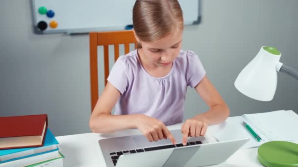 Дівчинка 7-8 років використовує ноутбук на столі і посміхається на камеру. Гаразд. Вид зверху — стокове відео