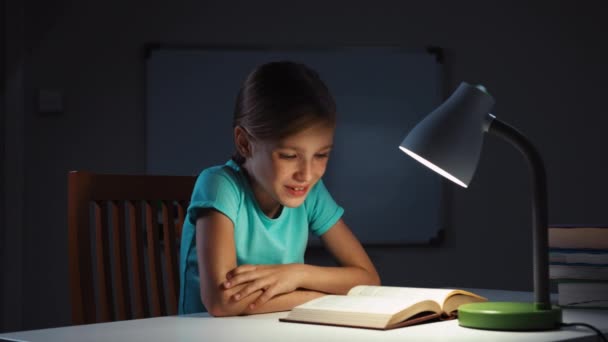 Ребенок читает книгу ночью и смеется над камерой — стоковое видео